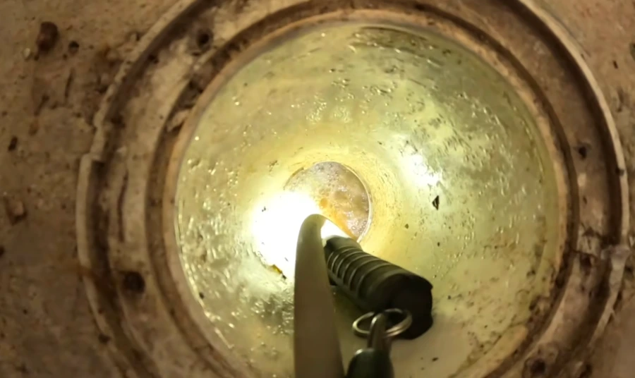 A large grease and root blockage sitting in standing water inside a brick lined sewer chamber, illustrating the kind of buildup found in aging Comstock area sewer lines