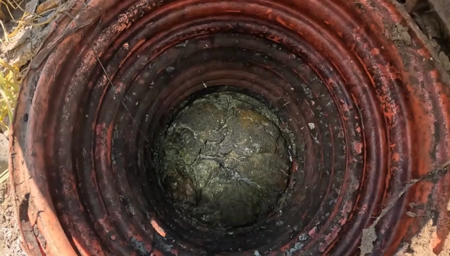 Looking straight down a corrugated pipe access shaft showing debris buildup, illustrating aging sewer pipe conditions in Brownes Addition