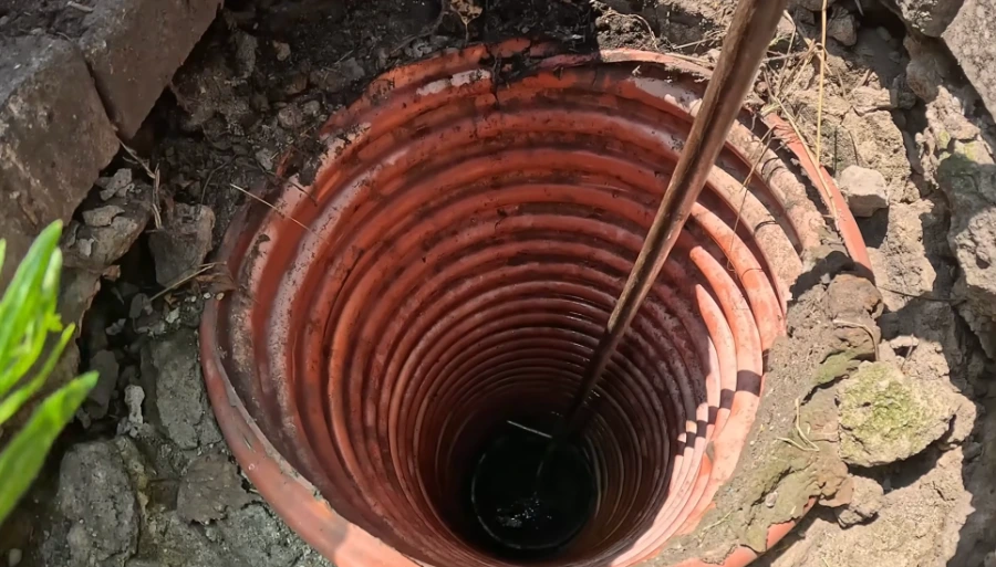 Looking down an old corrugated sewer access shaft toward dark standing water, illustrating the kind of aging pipe access common in older Spokane neighborhoods