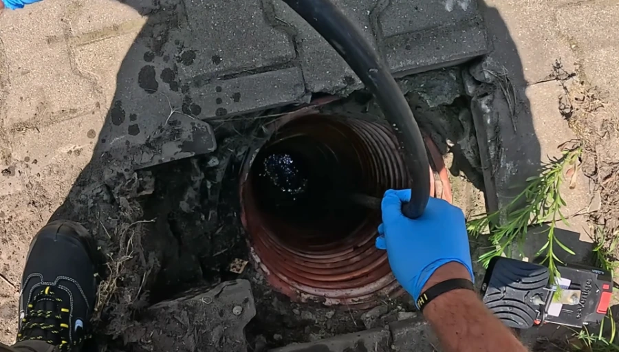 Looking down into a corrugated sewer access pipe with a cable being fed in by a gloved hand, illustrating trenchless access for a Spokane sewer line repair